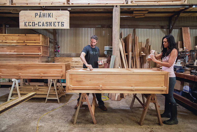 CINDY ELLEN RUSSELL / CRUSSELL@STARADVERTISER.COM
                                Owner Cortney Gusick and casket carpenter Logan Baggett apply an eco-friendly finish on an albizia casket in the company’s Waimanalo work space.