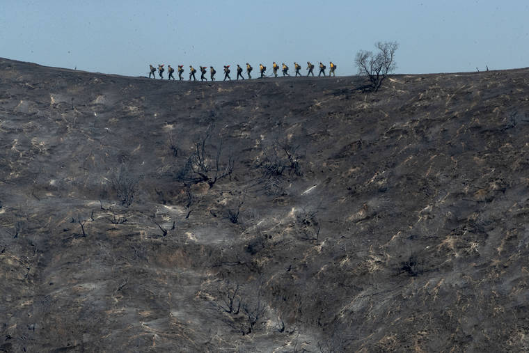 ASSOCIATED PRESS
                                Fire crews walk along a blackened ridge as they battle the Getty fire today.