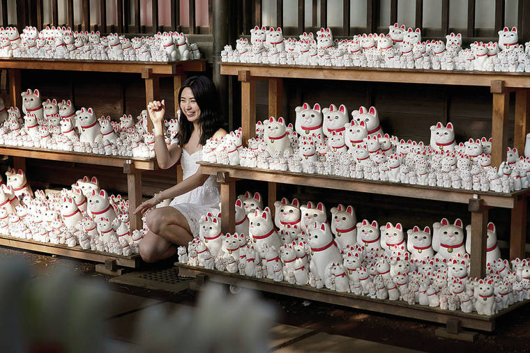 ASSOCIATED PRESS
                                A summer visitor posed with beckoning cat figurines at Gotokuji Temple in Tokyo.