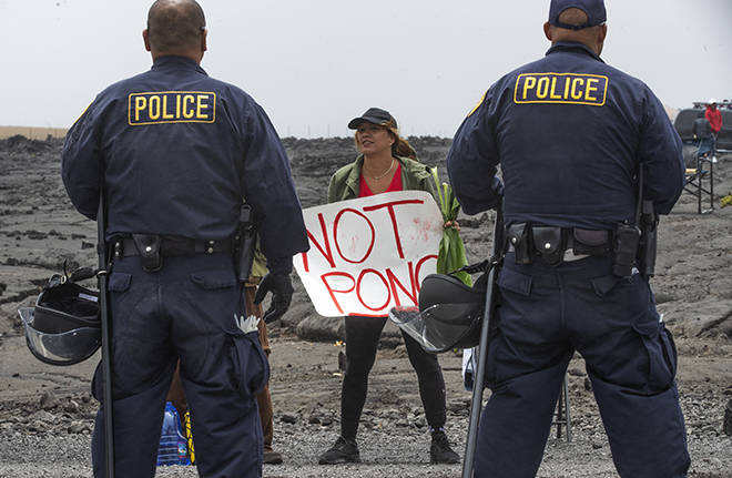 CINDY ELLEN RUSSELL / JULY 17
                                Police officers stand in front of a woman protesting the Thirty Meter Telescope on Mauna Kea Access Road in July. The state and counties have spent at least $9 million on law enforcement costs related to the protest, according to new figures released today.