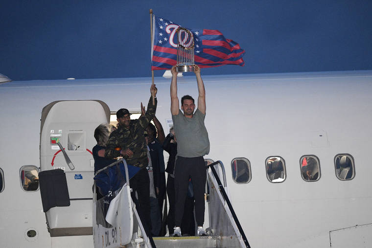 ASSOCIATED PRESS
                                Washington Nationals manager Dave Martinez, left, waves a flag and Ryan Zimmerman, right, hoists the World Series trophy as the baseball team arrives at Dulles Airport, in Chantilly, Va.
