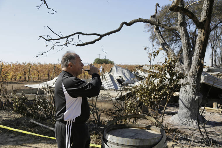ASSOCIATED PRESS / NOV. 6 Izzy Lewkosky, of Kansas City, Kan., tastes a glass of Cabernet Sauvignon while looking out at the wildfire incinerated Soda Rock Winery in Healdsburg, Calif. Despite a late October blaze that raged through one of the world’s best-known wine-growing regions, forcing evacuations in two mid-sized towns, wine production in Sonoma County escaped largely unscathed.