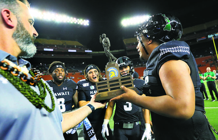 JAMM AQUINO / JAQUINO@STARADVERTISER.COM
                                Hawaii head coach Nick Rolovich, above left, handed the Dick Tomey Legacy Trophy to his players after the Rainbow Warriors’ win over San Jose State on Saturday at Aloha Stadium. The trophy is named after the former Hawaii and San Jose State coach.