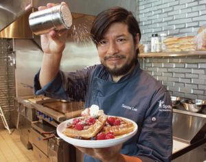 CRAIG T. KOJIMA /CKOJIMA@STARADVERTISER.COM
                                Santos Loo sprinkles powdered sugar over a waffle with fruit in Consolidated Theatres new Mililani kitchen.