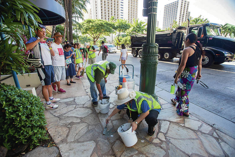 DENNIS ODA / DODA@STARADVERTISER.COM
                                Volunteers from local groups repair the sidewalk along Kuhio Avenue as Waikiki tourists watch. The city is providing the resources, and community volunteers work to identify and fix sidewalk hazards.