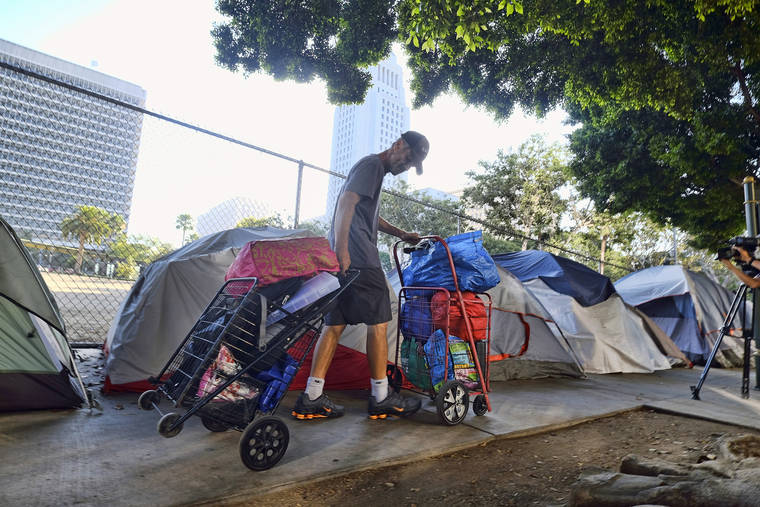 ASSOCIATED PRESS
                                A homeless man moved his belongings, in July 2019, from a street near Los Angeles City Hall, background, as crews prepared to clean the area. Los Angeles city and county officials on Tuesday announced a new strategy to speed the process of getting homeless people into permanent housing that is modeled on the federal government’s response to natural disasters.
