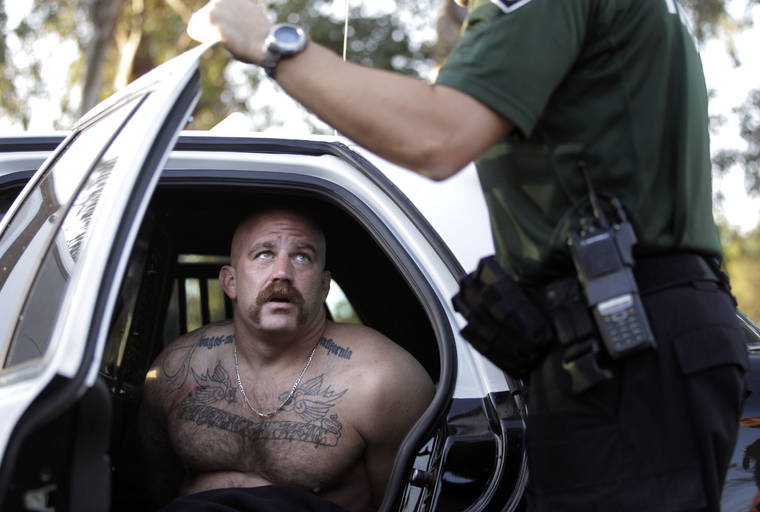 ASSOCIATED PRESS / Oct.16, 2011
                                Andrew Lozano, a member of the Vagos motorcycle gang, talks to a Fontana police officer after he was arrested in an early morning raid in Fontana, Calif., in October 2011.