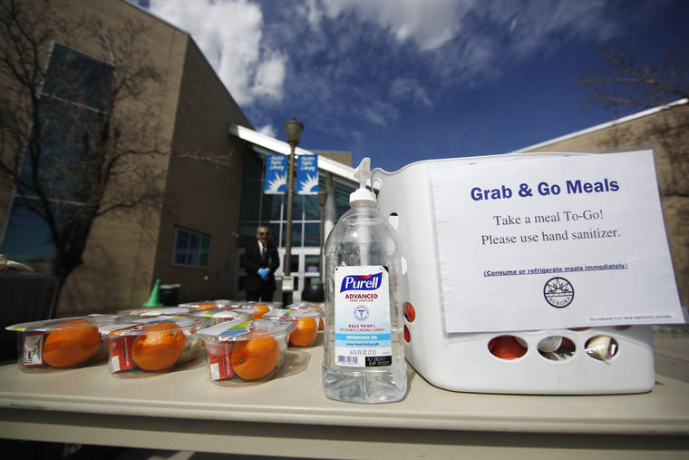 ASSOCIATED PRESS
                                A bottle of hand sanitizer stands next to free lunches for people under the age of 18 outside the Aurora Public Library as branch manager Phillip Challis, back, looks on in an effort to help city residents and reduce the spread of the new coronavirus today.