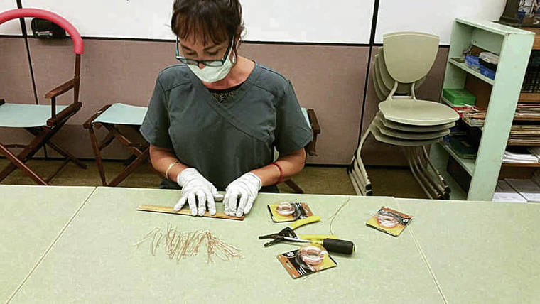 COURTESY JENNIFER OBERG
                                Kai Nishiki measures and cuts copper wire that will allow the masks to be molded around the nose for a snug fit. Those working on the project maintain a strict hygiene regimen that includes disinfecting all surfaces and equipment and wearing gloves, masks and medical “scrubs.”