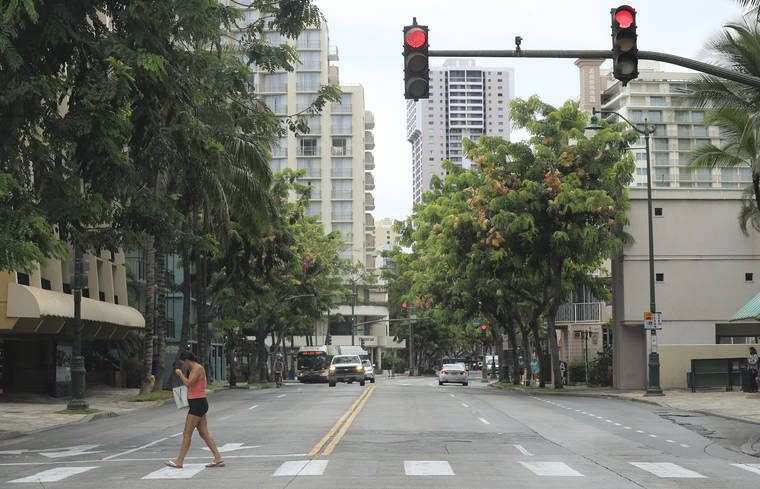 JAMM AQUINO / JULY 30
                                A woman walks across Kuhio Avenue in Waikiki. Though visitor arrivals continue at a steady pace despite the coronavirus pandemic and the 14-day mandatory quarantine, the predicted economic outlook still appears grim.