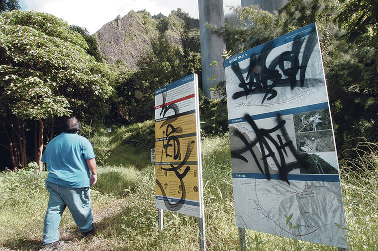 STAR-ADVERTISER / 2004
                                Junior Martinez, a Department of Parks and Recreation employee, in 2004 inspected the entry to the hike to the Haiku Stairs. The temporary signs at the start of the hike had been vandalized.
