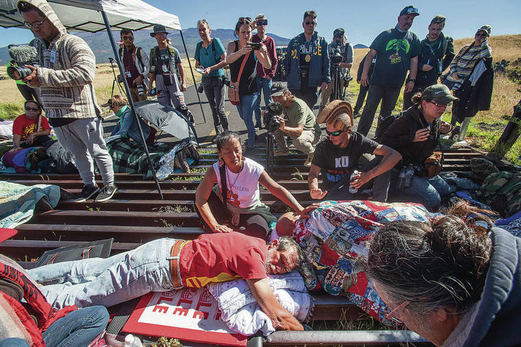 STAR-ADVERTISER / JULY 15, 2019
                                It has been a year since protesters gathered on Mauna Kea Access Road to block construction of the Thirty Meter Telescope. Above, supporters tend to Walter Ritte, left, and Kaleikoa Kaeo, who joined others who chained themselves to a cattle grate to form a human barricade.