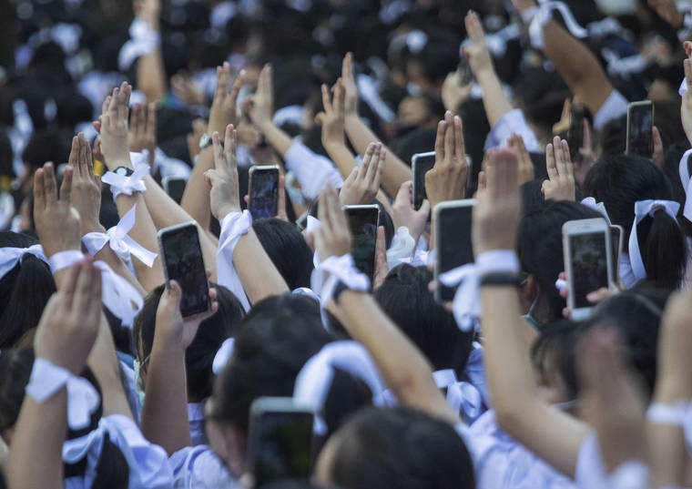 Pro-democracy students raise a three-fingers, symbol of resistance salute and their mobile phone during a protest rally in front of Education Ministry in Bangkok, Thailand, today. Student protesters have stepped up pressure on the government with three core demands: holding new elections, amending the constitution and ending the intimidation of critics of the government.