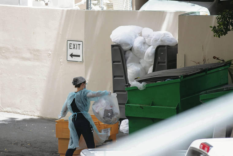 CINDY ELLEN RUSSELL / CRUSSELL@STARADVERTISER.COM
                                A worker in PPE disposed of bags of trash Sunday in the back of the the Pearl Hotel Waikiki. Also visible is the mound of dirty linens awaiting pick-up near a wall that separates the Pearl Hotel Waikiki from The Palms building.
