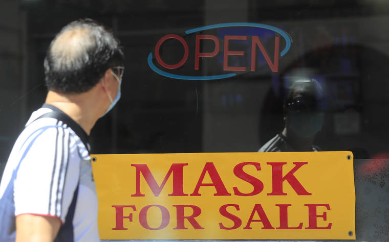 JAMM AQUINO / OCT. 24
                                A man wearing a face mask peers at a storefront sign advertising masks for sale along Maunakea Street.