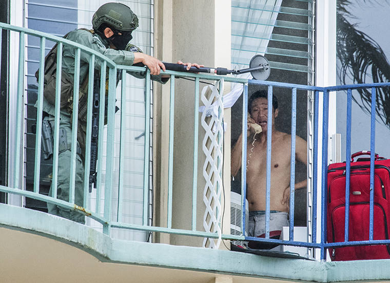 CRAIG T. KOJIMA / CKOJIMA@STARADVERTISER.COM An officer from the Honolulu Police Department uses a mirror to monitor the actions of a suspect today in Waikiki. The man, seen here on the phone, was subdued a few minutes later by police using a loud explosive device to enter the apartment at 1909 Ala Wai Blvd.