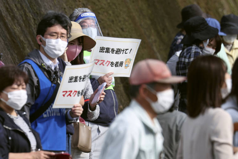 KYODO NEWS VIA ASSOCIATED PRESS
                                Organizers held signs to spectators that read: “Avoid crowding! Wear masks” during the Tokyo Olympic torch relay in Tobe, Ehime prefecture, southwestern Japan, Thursday. Tokyo Olympic organizers said, Thursday, that a Japanese policeman tested positive for COVID-19 a day after his assignment of traffic control at the April 17 leg of the torch relay.