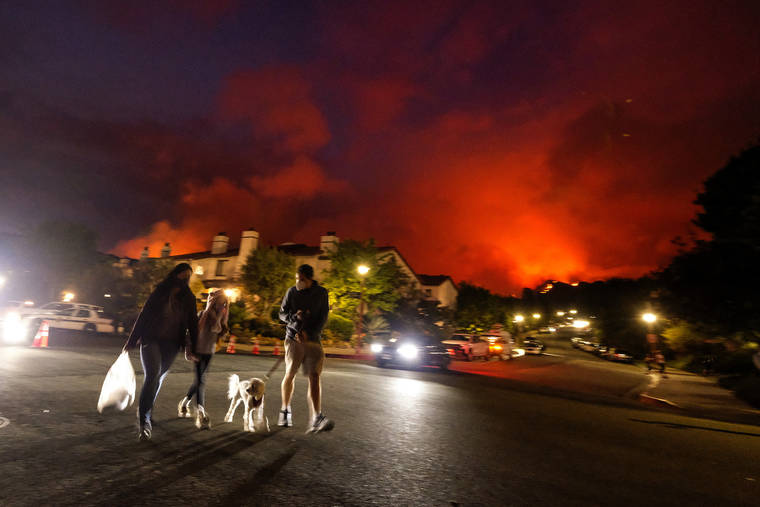 ASSOCIATED PRESS
                                Residents walk a dog as a brush fire burns behind homes in the Pacific Palisades area of Los Angeles on Saturday.
