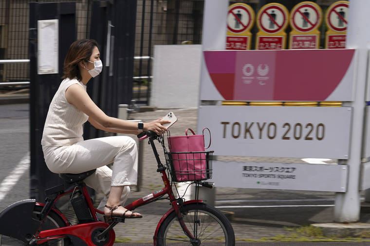 ASSOCIATED PRESS
                                A woman wearing a protective mask rides a bicycle past a banner for the Tokyo 2020 Olympic and Paralympic Games in Tokyo.
