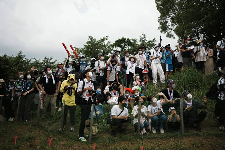 ASSOCIATED PRESS
                                Masked fans watch from a hillside during the men’s cross country mountain bike competition on Monday in Izu, Japan.
