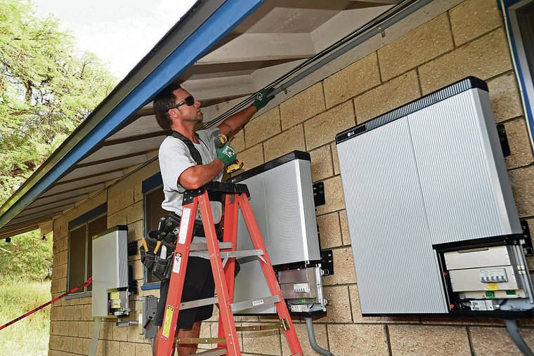 STAR-ADVERTISER / 2019
                                Hawaiian Electric has begun taking applications for its new solar battery program. Above, Justin Brennan puts up an electrical conduit near three battery modules during a solar panel system home installation in Waianae.