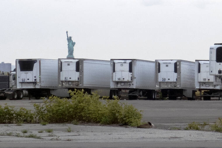 ASSOCIATED PRESS / MAY 6, 2020
                                The Statue of Liberty rises in the distance above trucks at a temporary morgue in Brooklyn in the early days of the coronavirus pandemic.