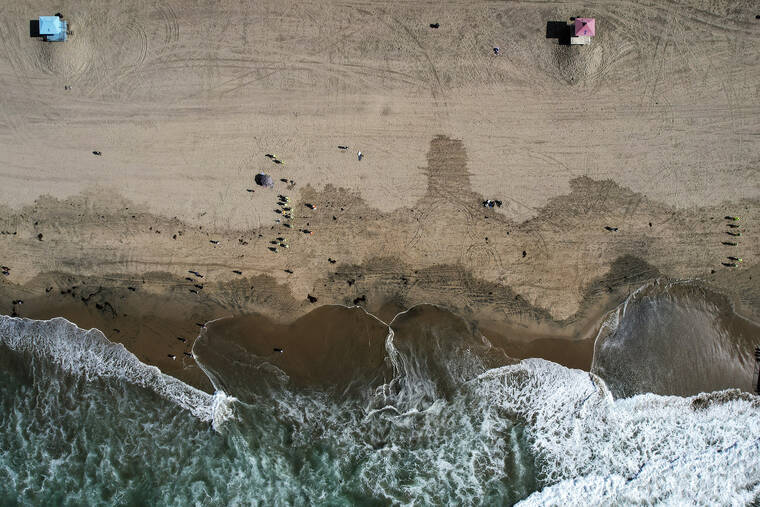 ASSOCIATED PRESS
                                This aerial photo taken with a drone, shows beachgoers as workers in protective suits continue to clean the contaminated beach in Huntington Beach, Calif., on Oct. 11. Officials were investigating an oil sheen spotted Saturday near last month’s crude pipeline leak off Southern California’s coast. The U.S. Coast Guard said in a statement the oil sheen is about 70 feet by 30 feet and that it has dispatched “pollution responders, aircraft and boats” to investigate.