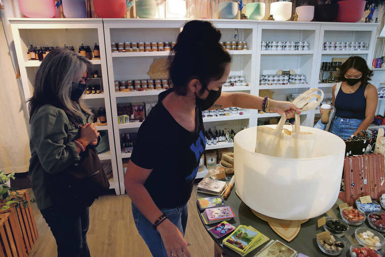 JAMM AQUINO / JAQUINO@STARADVERTISER.COM
                                House of Intention sales associate Noelle Holi, center, charged items purchased by Lisa Char, left, with positive energy during Small Business Saturday. The Kaimuki shop sells aromatic candles, crystals, gems and other holistic trinkets.