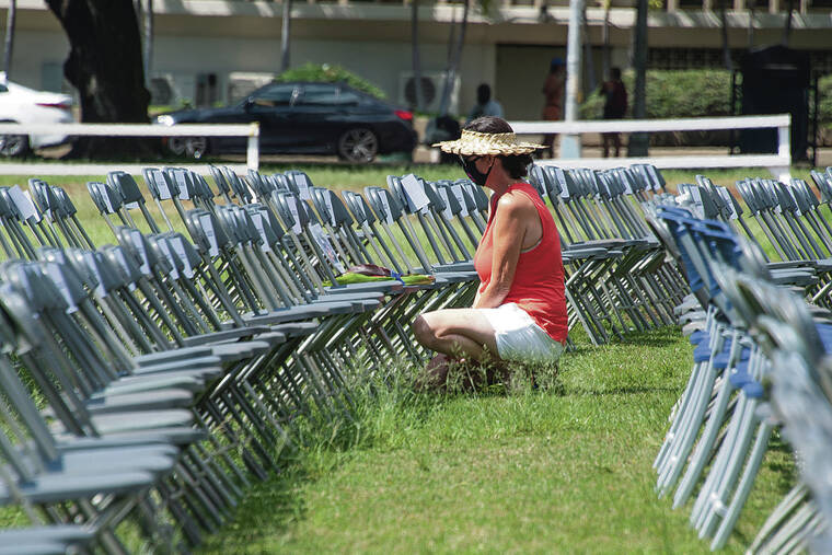 CRAIG T. KOJIMA / CKOJIMA@STARADVERTISER.COM
                                Alice Taum offered flowers Monday for a neighbor and friend’s husband on chairs on the front lawn of Central Union Church. Each chair represents a person in Hawaii who has died from COVID-19.
