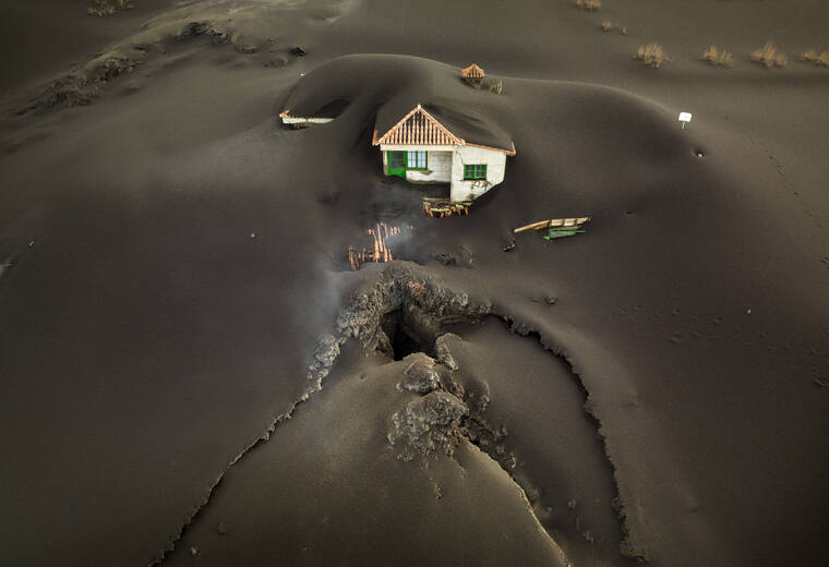 ASSOCIATED PRESS
                                A fissure was seen next to a house covered with ash on the Canary island of La Palma, Spain, today. Volcanologists believe the fissure spouted a gusher of lava and left a gaping hole in front of the house whose bottom floor was completely covered by a mountain of ash.