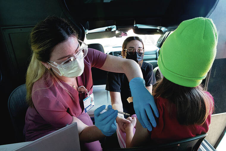 GEORGE F. LEE / GLEE@STARADVERTISER.COM
                                Hawaii Pacific Health held a mobile COVID-19 vaccination clinic at Red Hill Elementary School on Wednesday. Erica Ham administered the shot as Alexis Schultz distracted 9-year-old Izzy Pratt.