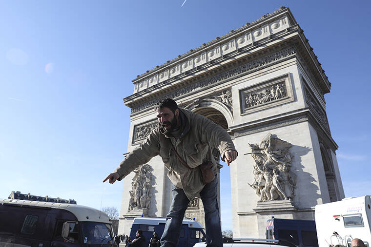 ADRIENNE SURPRENANT / AP
                                A protester stands atop a vehicle as the convoy drives past the Arc de Triomphe on the Champs-Elysees avenue in Paris.