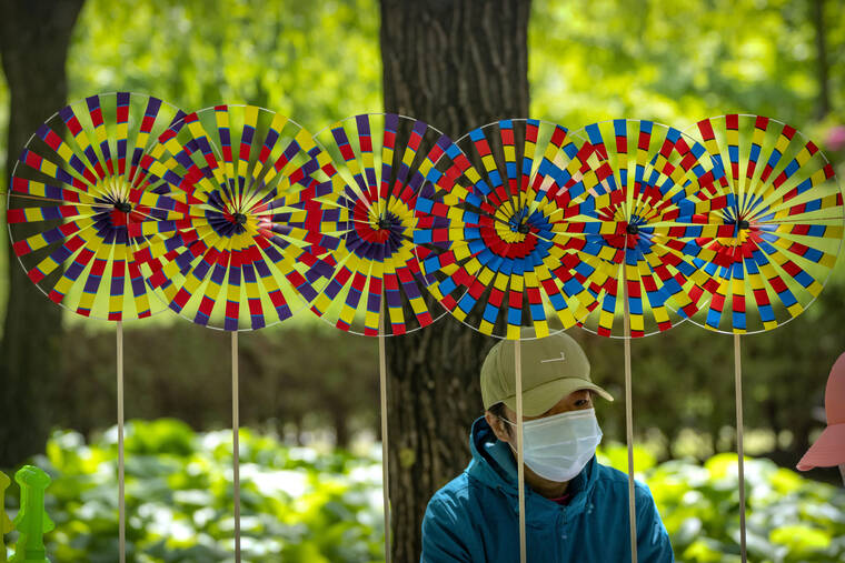 MARK SCHIEFELBEIN / AP
                                A vendor wearing a face mask sits near pinwheels for sale at a public park in Beijing Saturday, the first day of the Labor Day holiday period in China.