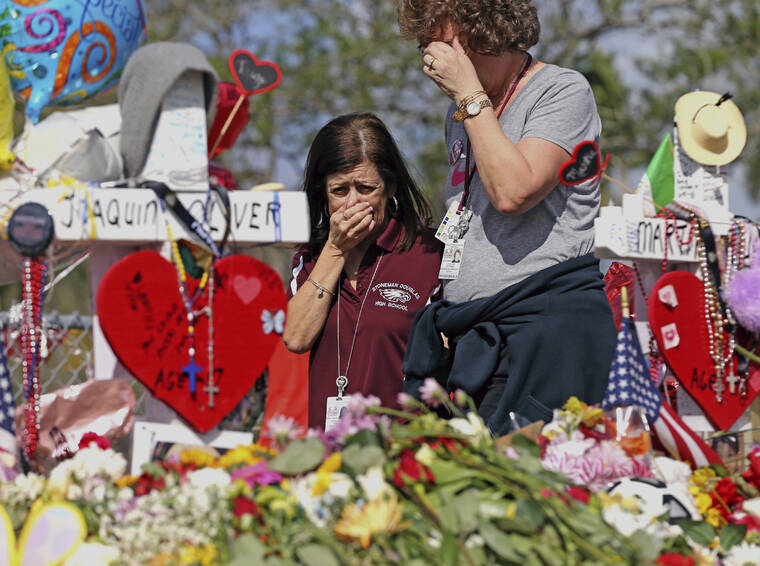 CHARLES TRAINOR JR/MIAMI HERALD VIA AP / 2018
                                Marjory Stoneman Douglas High School administrative employees Margarita LaSalle, left, and JoEllen Berman, walk along the hill near the school lined with 17 crosses to honor the students and teachers killed on Valentine’s Day, as teachers and staff returned to the school in Parkland, Fla.