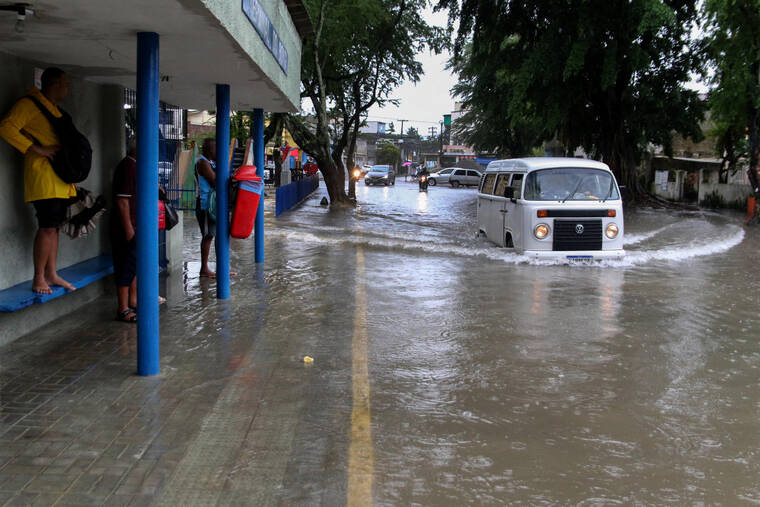 FUTURA PRESS / AP
                                A woman stands on a bus stop bench as a driver of a Volkswagen van navigates a flooded street in Recife, state of Pernambuco, Brazil, Saturday.