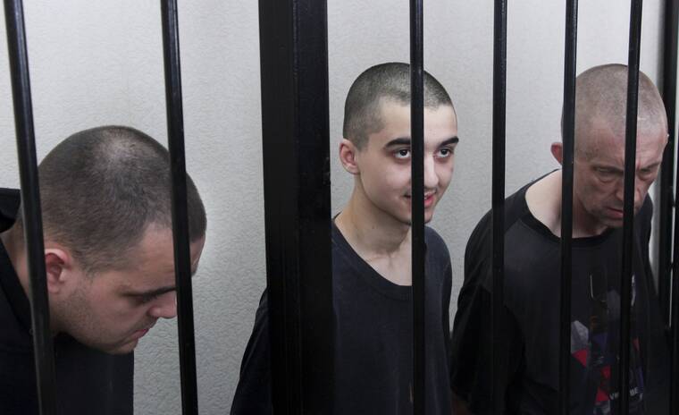 ASSOCIATED PRESS / JUNE 9
                                Two British citizens Aiden Aslin, left, and Shaun Pinner, right, and Moroccan Saaudun Brahim, center, sit behind bars in a courtroom in Donetsk, in the territory which is under the Government of the Donetsk People’s Republic control, eastern Ukraine. The two British citizens and a Moroccan have been sentenced to death by pro-Moscow rebels in eastern Ukraine for fighting on Ukraine’s side. The three men fought alongside Ukrainian troops and surrendered to Russian forces weeks ago.