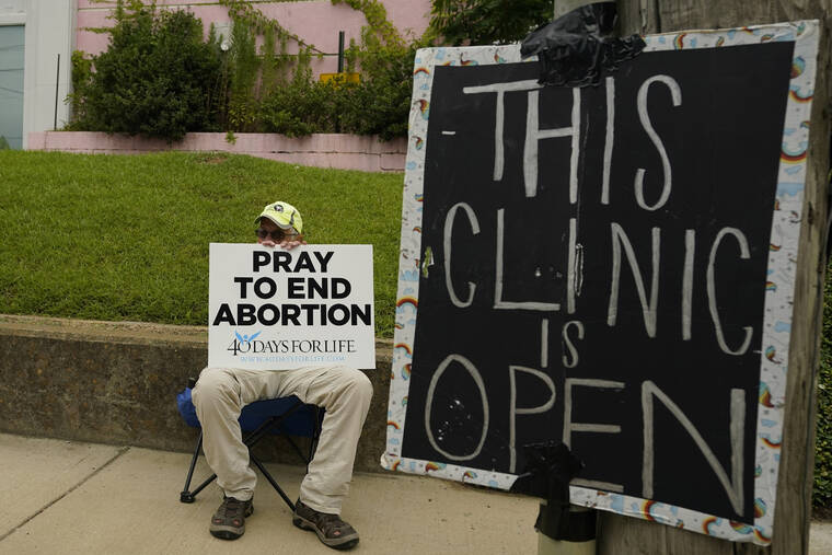 ROGELIO V. SOLIS / AP
                                An anti-abortion supporter sits behind a sign that advises the Jackson Women’s Health Organization clinic is still open in Jackson, Miss., Wednesday.