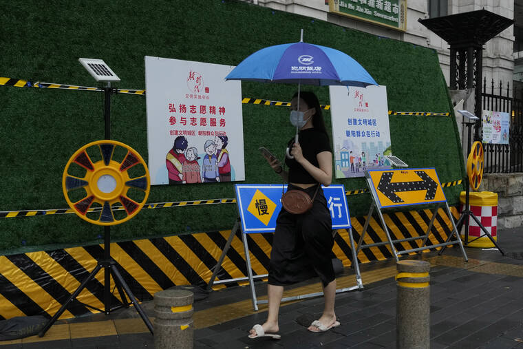 ASSOCIATED PRESS
                                A woman wearing a mask walks past a construction warning sign during a rainy day in Beijing.